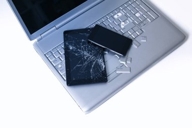 Kırık klavyeye sahip gümüş bir dizüstü bilgisayar, kırık ekranlı tablet ve siyah telefon. Tablette bozuk dizüstü bilgisayar ve kırık ekranın bir kısmının yakın çekim resmi.