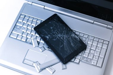 Kırık klavyeye sahip gümüş bir dizüstü bilgisayar, kırık ekranlı tablet ve siyah telefon. Tablette bozuk dizüstü bilgisayar ve kırık ekranın bir kısmının yakın çekim resmi.