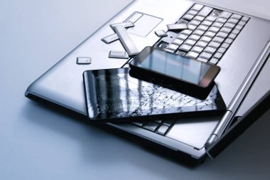 Kırık klavyeye sahip gümüş bir dizüstü bilgisayar, kırık ekranlı tablet ve siyah telefon. Tablette bozuk dizüstü bilgisayar ve kırık ekranın bir kısmının yakın çekim resmi.