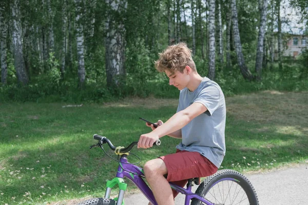 Curly teenager boy riding a bike and texting. — Stock Photo, Image