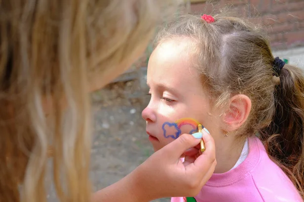 Artista pintando um arco-íris no rosto das meninas . — Fotografia de Stock