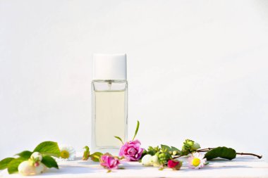 Beyaz ahşap tepside beyaz ve pembe çiçekli çiçek parfümü şişesi. Çiçek parfümü sunumu için markasız parfüm. Doğanın kokusu. Ön manzara. ev aromatizörleri. seçici odak