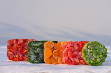 Ahşap masada donmuş sebzeler. Kış için vitamin sebzeleri hasat edip saklıyorum. Donmuş havuç, yeşil bezelye, domates ve dolmalık biber. Sağlıklı gıda deposu. Boşluğu kopyala.