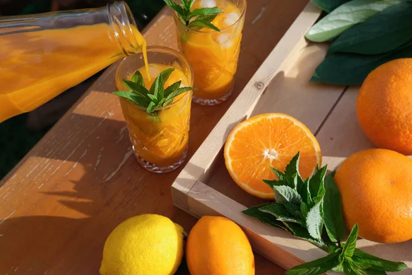 orange juice in crystal glasses with mint leaves and ice cubes. fresh citrus juice and oranges on a table. summer garden party. backyard party time. fruit juices as vitamin source.