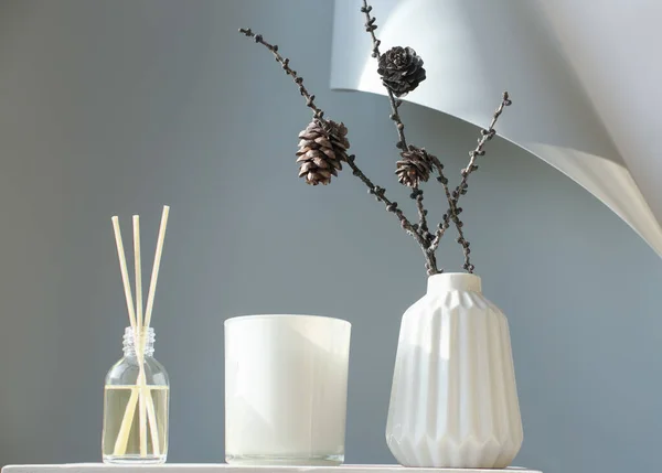 minimal style home decor. autumn or winter nordic design. hipster decoration style. reed diffuser, soy candle and white vase with larch cones. monochrome acsessories for trendy uncluttered room