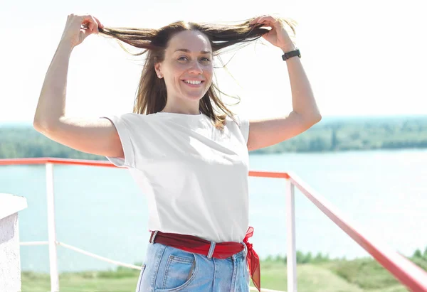 happy middle age woman smiling and showing her hair. beautiful woman wearing white t-shirt and jeans standing on a terrace on a river bank.