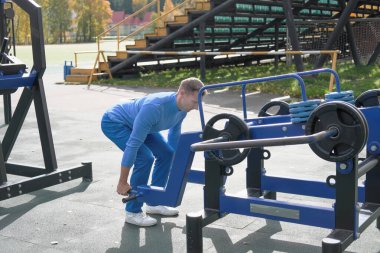 Orta yaşlı, beyaz bir adam kaldırma yapıyor. Spor aletlerini kullanarak. Sonbahar ya da açık hava sporu. aktif yaşam tarzı. Açık hava stadyum spor sahası. seçici odak