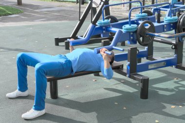 Spor spikeri, spor aletlerini kullanarak göğüs presi yapıyor. Çıtayı yükseltmek için çaba sarf ediyor. Motivasyon ve ilerleme kavramı. Göğüs egzersizi. Açık hava spor salonu
