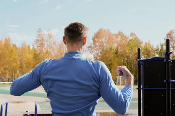 back view of a toned sporty man showing his muscules. autumn or fall stadium. sporty guy before workout, outdoors activity.