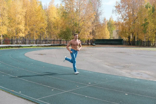Deportista sin camisa hombre corriendo en un estadio en la temporada de otoño. — Foto de Stock
