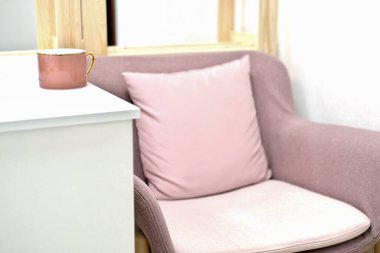 Beyaz masanın yanındaki rahat pembe koltuk. Pembe kahve fincanı. Kahve molası zamanı. Rahatlamak ve dinlenmek için sakin bir yer. Modern tarz dekorasyon için ev tasarımı ve oda mobilyaları.