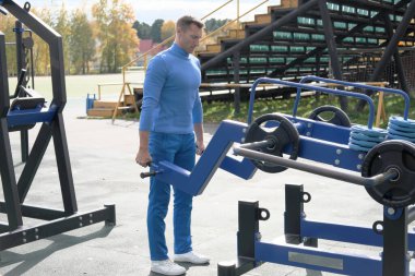 Spor kıyafetli yakışıklı adam sokak sporu malzemelerini kullanarak kaldırma yapıyor. Sonbahar sezonunda bir stadyumda formda ve zayıf bir adam antrenmanı. Açık hava eğitimi. 