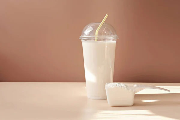 front view of whey protein cocktail in a disposable cup and scoop of collagen powder on a beige background. collagen peptides drink for joints and beauty. protein shake in take away cup.