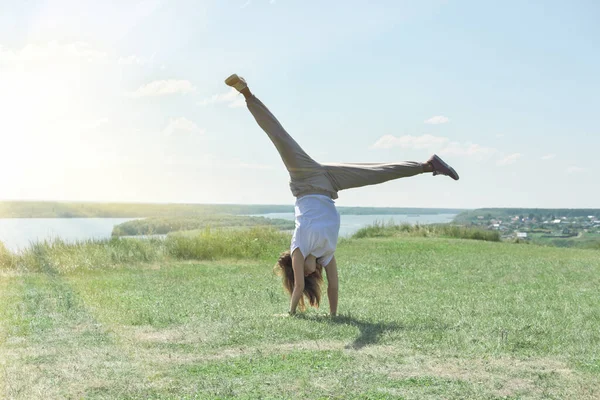 toned fit woman of mid age turning handsprings or cartwheel on a river bank. sunny weather and pleasant landscape. cheerful mood. outdoors workout and gymnastics.