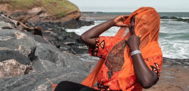 Sekondi-Takoradi Gana 'daki uçurumlarda turuncu elbiseli Afrikalı kadın. Batı Afrika.