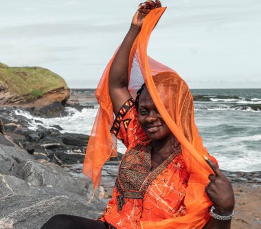 Sekondi-Takoradi Gana 'daki uçurumlarda turuncu elbiseli Afrikalı kadın. Batı Afrika.