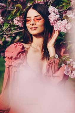 güzel bir genç kadının portresi, pembe çiçek açan bir ağacın yakınında, güzel bir gülümseme. Yaz parkında güzel kız.