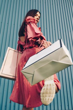 Alışveriş çantaları ile poz güneş gözlüğü giyen ve mavi arka plan üzerinde kenara bakarak beyaz yazlık elbise güzel bir genç esmer kadın Fotoğraf