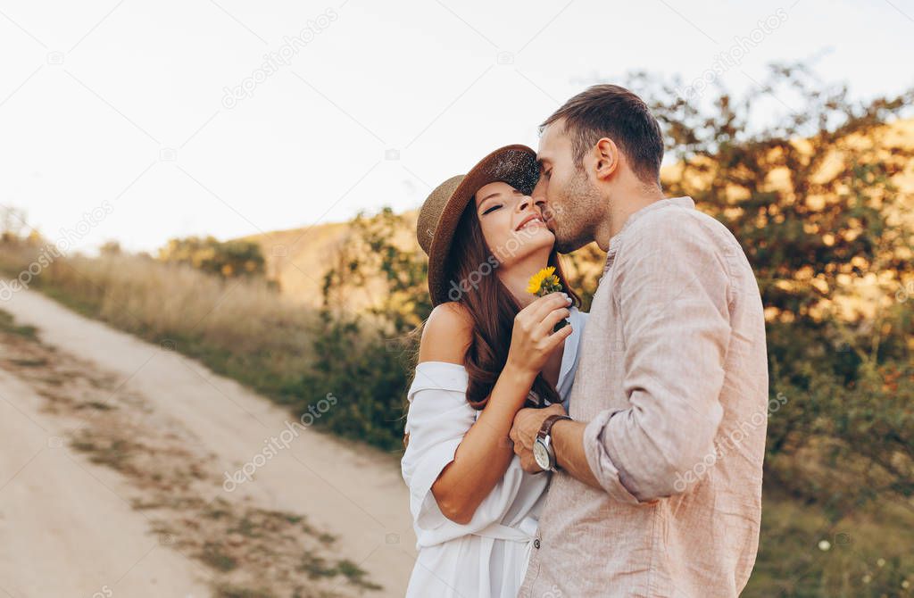 Stylish couple walking outdoors in lawn with a glass of wine. Man and woman looking at each other and walking together outdoors.