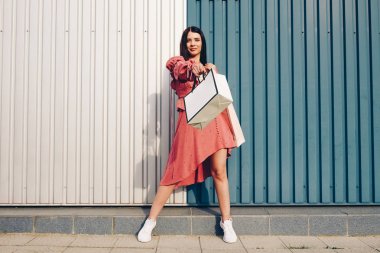 Genç ve hoş bir bayan, alışverişle mutlu. Yaz cebinde giyin ve çantalarını al. Metin yerleştirme yeri