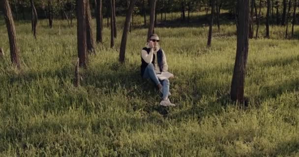 Troskliwy człowiek siedzi na trawie w lesie i czyta książkę — Wideo stockowe