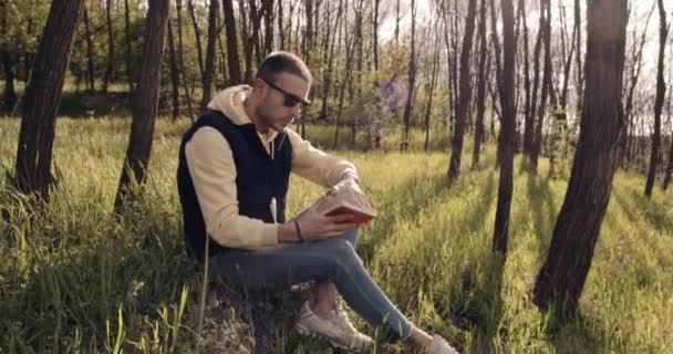 Troskliwy człowiek siedzi na trawie w lesie i czyta książkę — Wideo stockowe