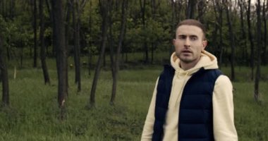 Kapüşonlu giyinmiş bir adam parkta, ormanda yürüyor.