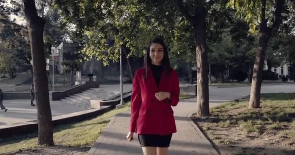 Mujer cruzando la calle mientras sostiene el teléfono inteligente y mirando hacia los lados . — Vídeos de Stock