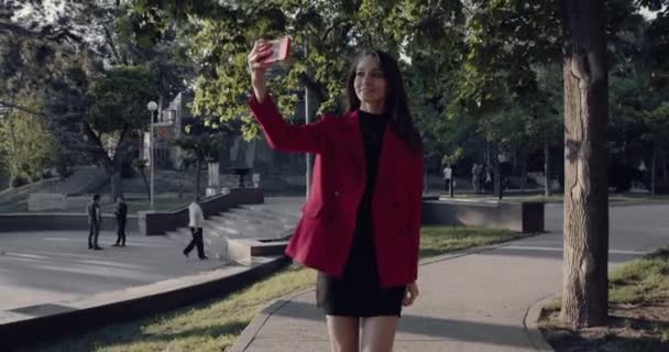 Mujer cruzando la calle mientras sostiene el teléfono inteligente y mirando hacia los lados . — Vídeos de Stock