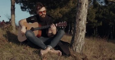 Sakallı bir adam gitar çalıyor.