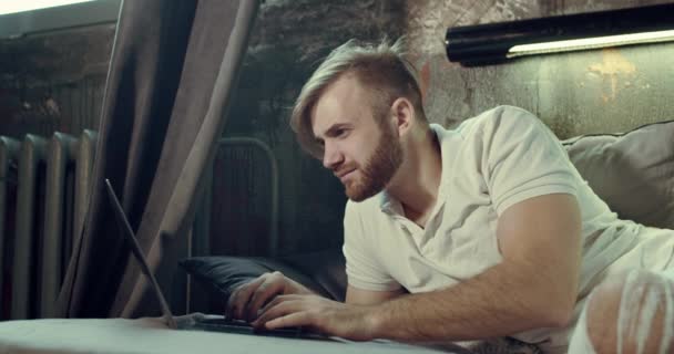 A close-up of a bearded man typing on the Laptop sitting in his comfortable bed — Stock Video