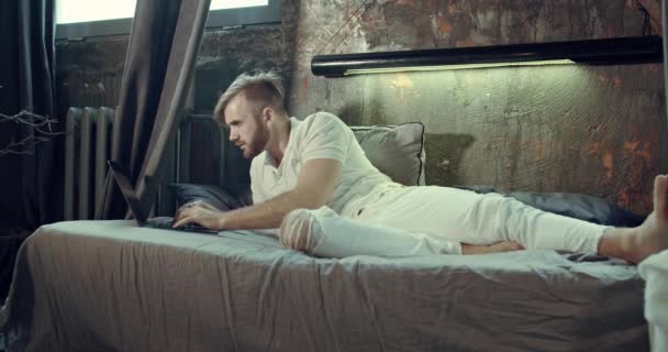 Ένας άντρας θέλει να αγοράσει ρούχα στο ίντερνετ, κάθεται στο άνετο κρεβάτι του.. — Αρχείο Βίντεο