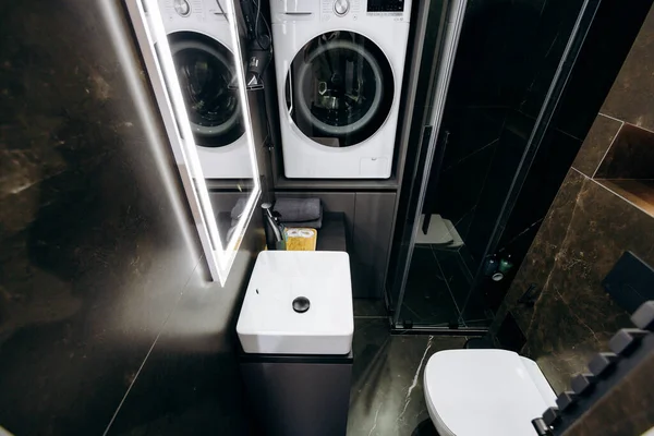 Bu modern banyo tasarımı gelişmiş bir estetik için kompakt bir çamaşır makinesi, kurutucu, tuvalet ve şık kaplamalar içerir.