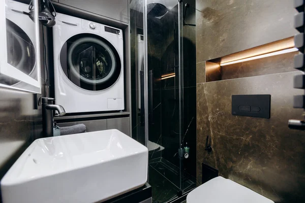 Bu çağdaş banyo bir çamaşır makinesi sergiliyor, zarif bir tasarım ve zarif eşyalar içeriyor.