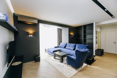 Modern ve çağdaş bir oturma odası, rahat mavi bir kanepe, şık bir dekor ve bol miktarda parlak doğal ışık içerir.