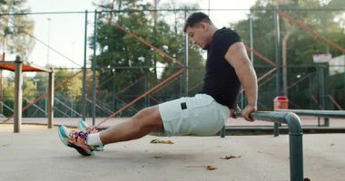 A dedicated athlete passionately performs dips for strength training at a local park gym in an outdoor environment