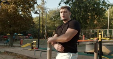 A strong and youthful man confidently poses in a lovely park that is surrounded by vibrant autumn scenery