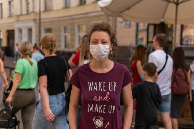 Maskeli genç bir kız sokakta kalabalığın içinde duruyor. Bir sürü insan maskeli geziyor.