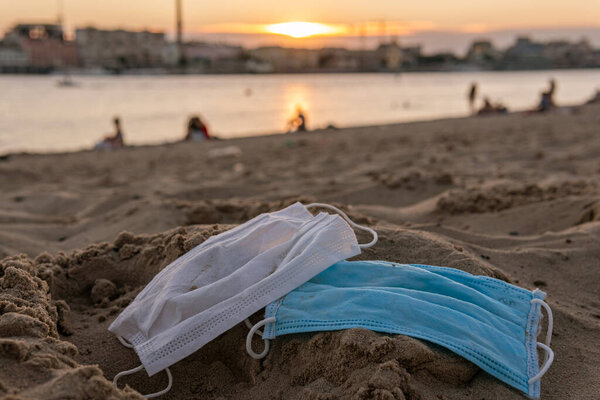 Две используемые одноразовые маски (защищенные от COVID-19, коронавируса) находятся на пляже, покрытом песком, что приводит к плохим последствиям, таким как загрязнение или загрязнение природы и воды.
