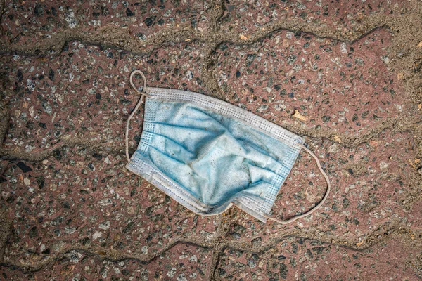 A used dirty disposable mask (protects from COVID-19, Coronavirus) is on a street