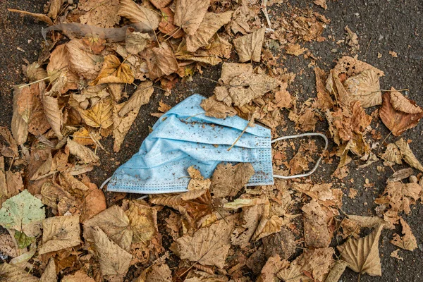 Sonbaharda sarı yaprakların arasında kirli, tek kullanımlık bir maske duruyor.