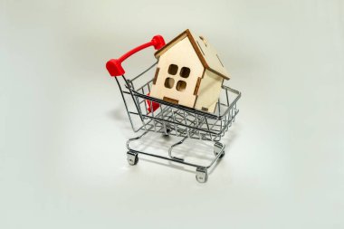 İpotek konsepti. Ev alışverişi. Oyuncak alışveriş arabası olan ahşap bir evin küçük bir modeli..