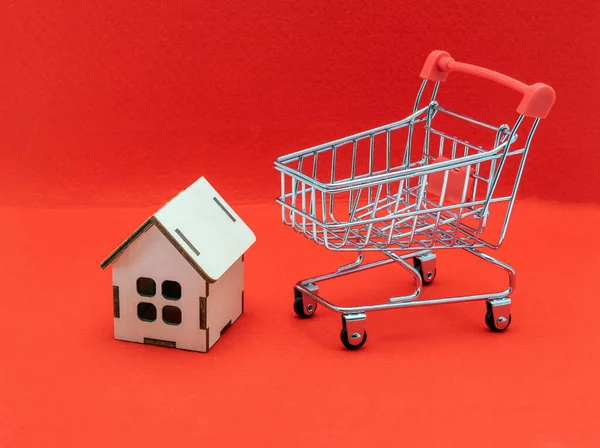Real estate sales and realtor services. Buying a new home and housing, concept. A small model of a wooden house with a toy shopping cart.