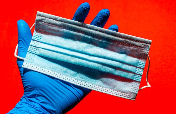 Disposable surgical mask in the doctors hand on a red background