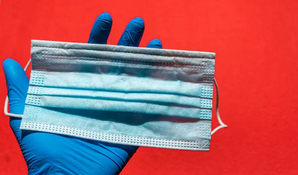 Disposable surgical face mask in hand with a surgical glove on a red background — Stock Photo, Image