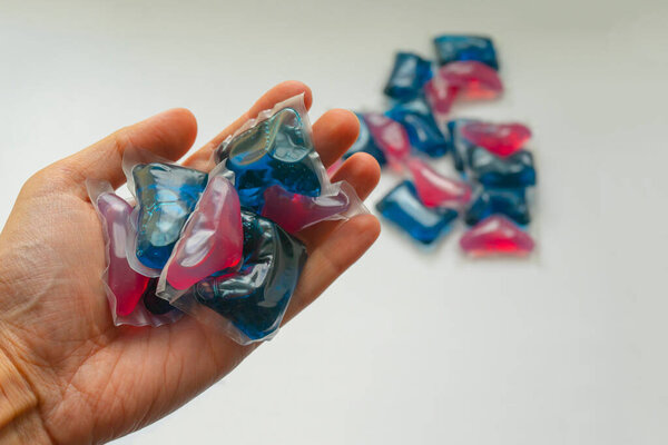 blue and red gel capsules for delicate washing on the palm of a man's hand. Capsules for washing clothes and clothes