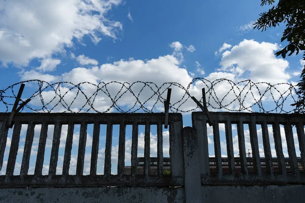 Beton bir çitin üzerindeki dikenli teller mavi gökyüzüne karşı. Koruma Alanı.