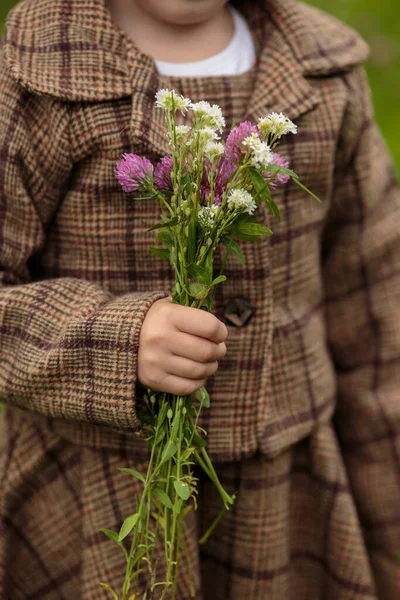 A little cheerful girl with a bouquet of wildflowers in a brown costume — Stock Photo, Image