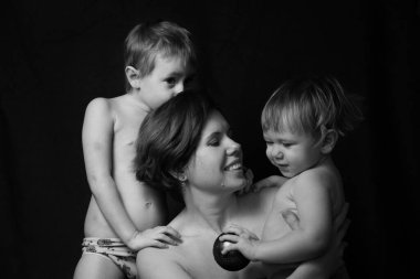 Siyah arka planda sevimli küçük çocukları olan sevimli, genç bir anne.