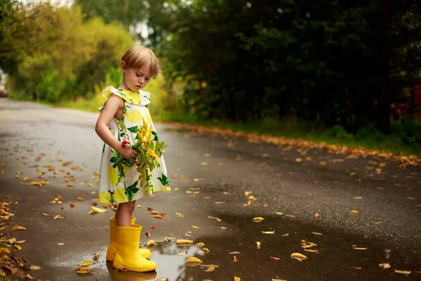 Pequena menina loira em um vestido colorido com uma lata de rega amarela sorrindo — Fotografia de Stock